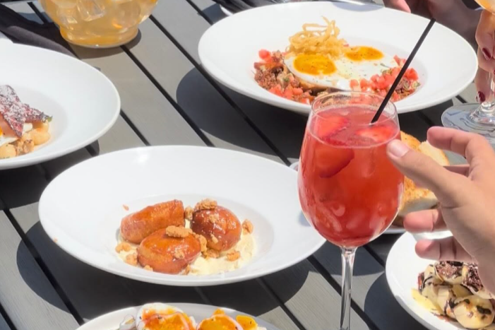 outdoor dining table with plates full of various brunch foods and a mimosa